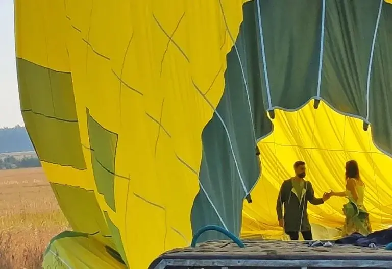 Two people standing next to a yellow hot air balloon are experiencing the joy of ballooning.