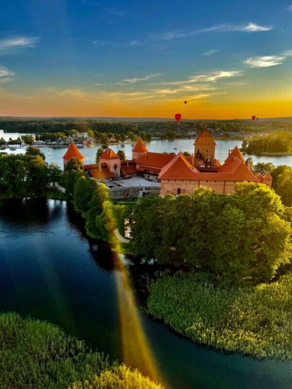 An aerial view of a castle on a lake with hot air balloons.
