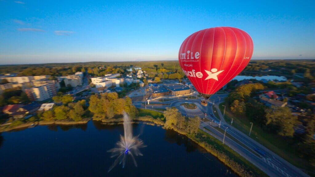 A red hot air balloon gracefully soaring above a bustling city.