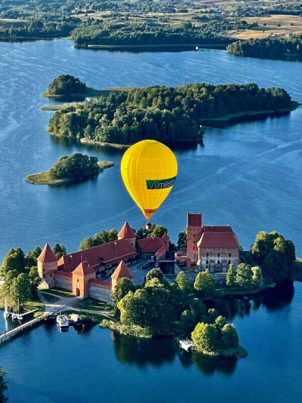 A hot air balloon floats over a castle on an island.
