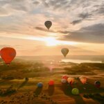 Grupė karšto oro balionų, skraidančių virš lauko saulėlydžio metu, skrydis oro balionu stebuklas.